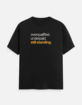 “overqualified. underpaid. still standing.” typography t-shirt in black by Halant, front