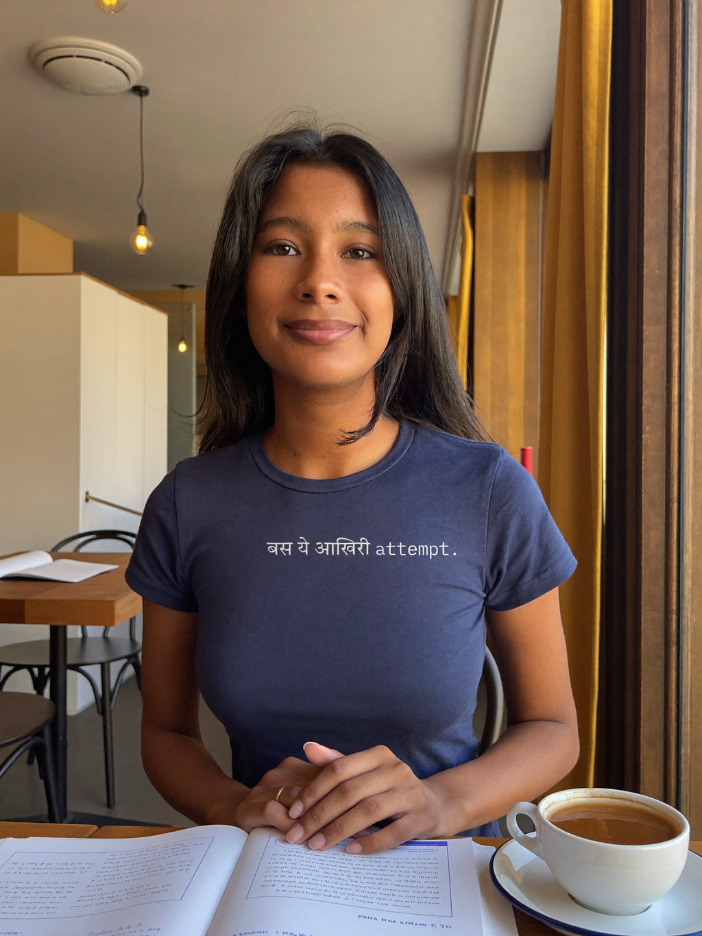 Woman wearing the “बस ये आखिरी attempt.” Hindi text t-shirt in navy by Halant, cafe