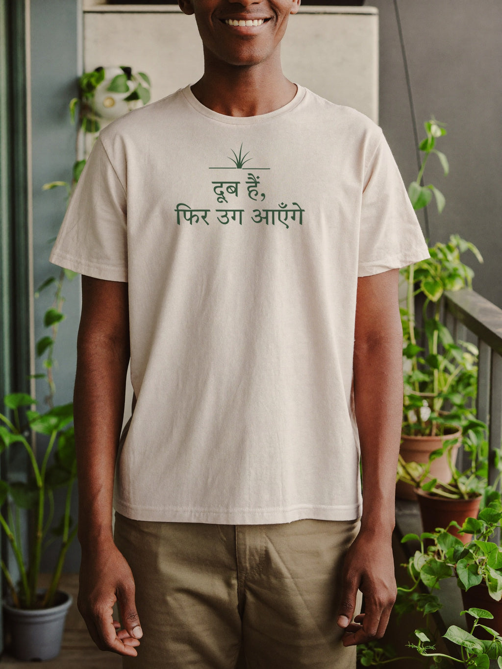 Man wearing the “दूब हैं, फिर उग आएँगे” t-shirt by Halant, plant balcony