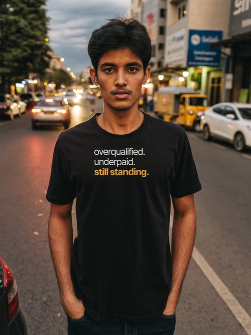 Man wearing the “overqualified. underpaid. still standing.” typography t-shirt in black by Halant on a Bangalore street