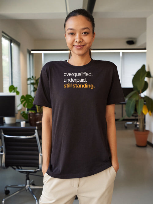 Woman wearing the “overqualified. underpaid. still standing.” typography t-shirt in black by Halant at the office